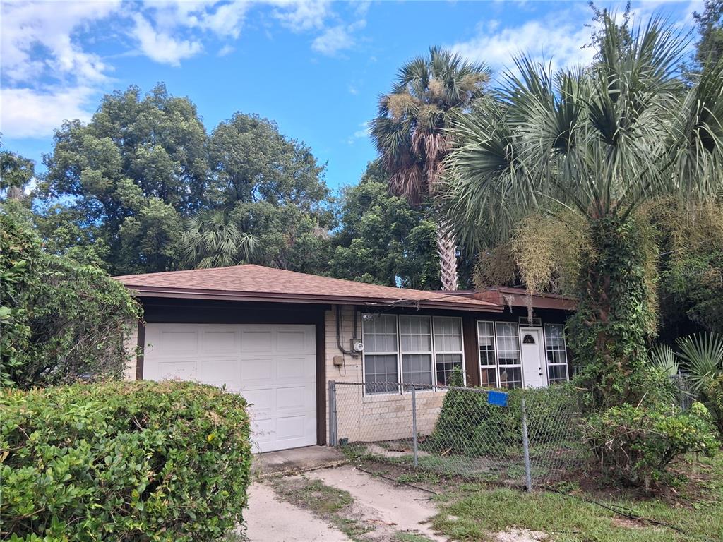 A single-story house with a white garage door, tan brick siding, and surrounding palm trees — 1326 NW 14TH AVENUE, GAINESVILLE, FL