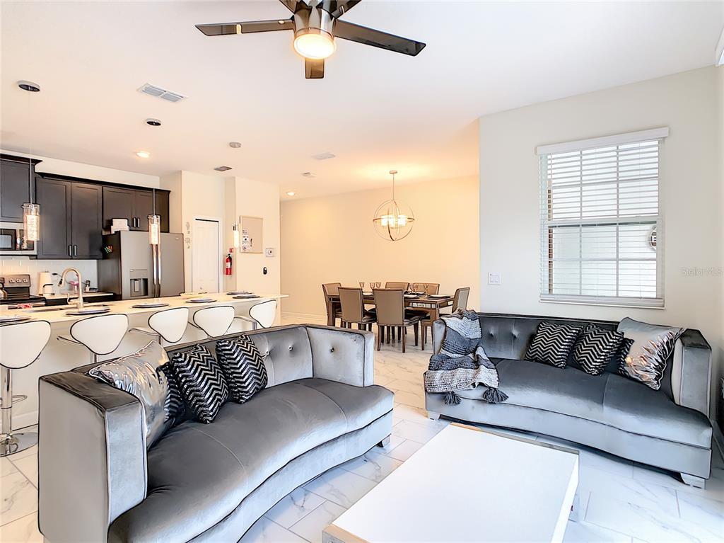 An open-concept living room and kitchen feature gray velvet sofas, white tile floors, and cabinetry — 4807 DEDICATION STREET, KISSIMMEE, FL
