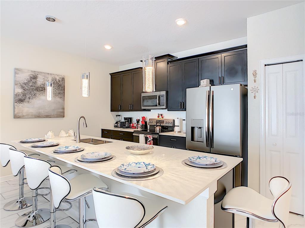 A modern kitchen features a large white island with bar seating and dark cabinetry — 4807 DEDICATION STREET, KISSIMMEE, FL