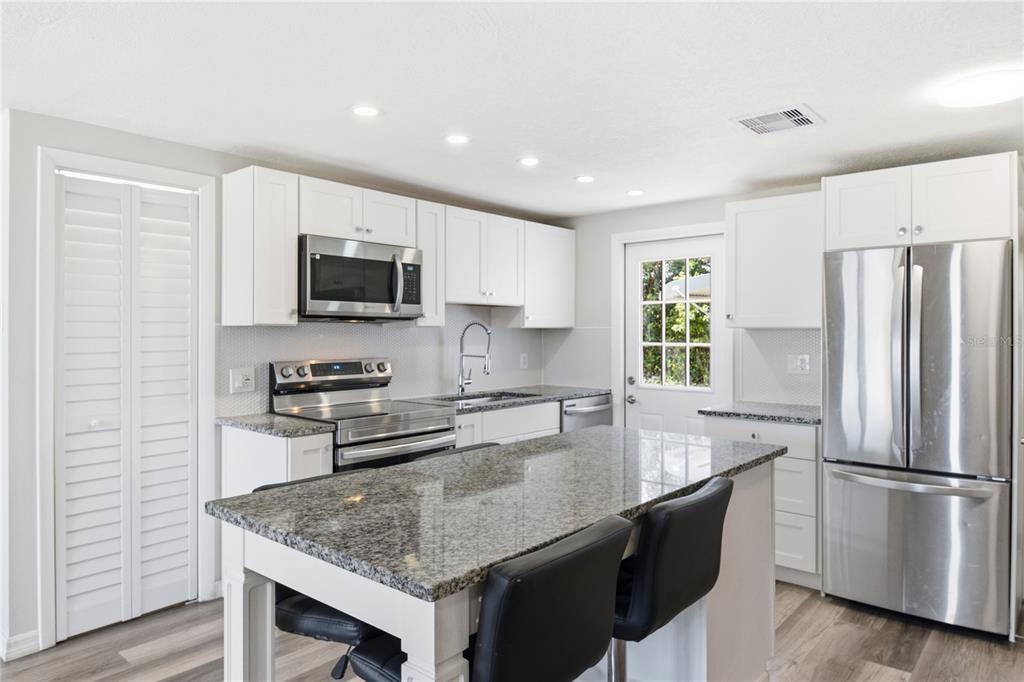 A kitchen features white cabinets, granite countertops, stainless steel appliances, and a central island — 4810 GUARDIAN AVENUE, HOLIDAY, FL