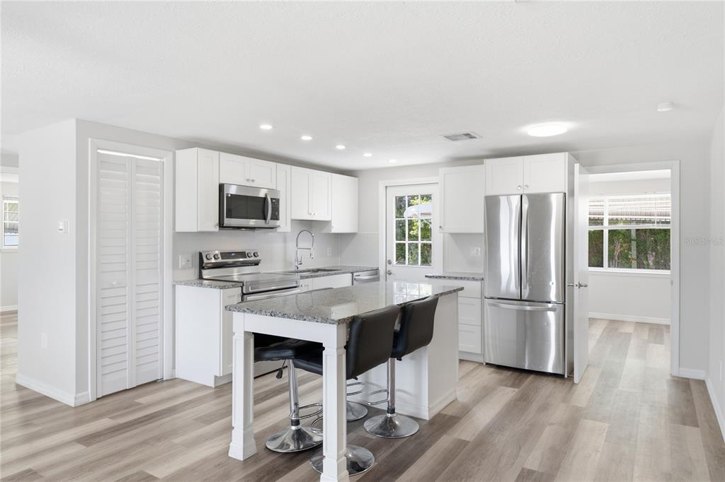 A modern kitchen features white cabinets, granite countertops, stainless steel appliances, and a central island — 4810 GUARDIAN AVENUE, HOLIDAY, FL
