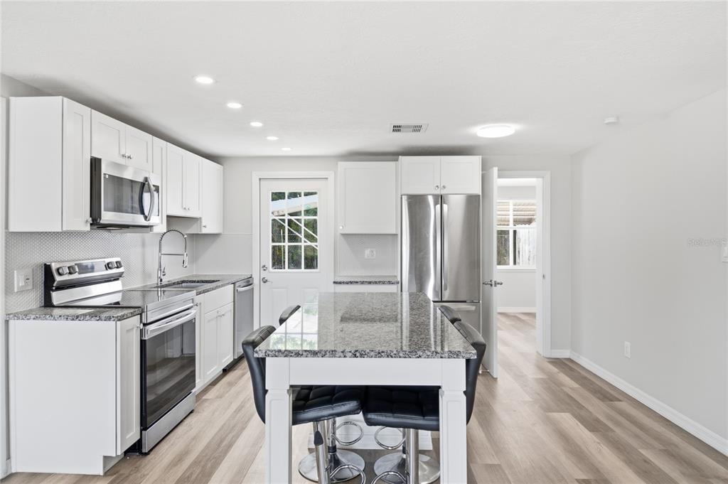 A modern kitchen features white cabinets, granite countertops, a central island, and stainless steel appliances — 4810 GUARDIAN AVENUE, HOLIDAY, FL