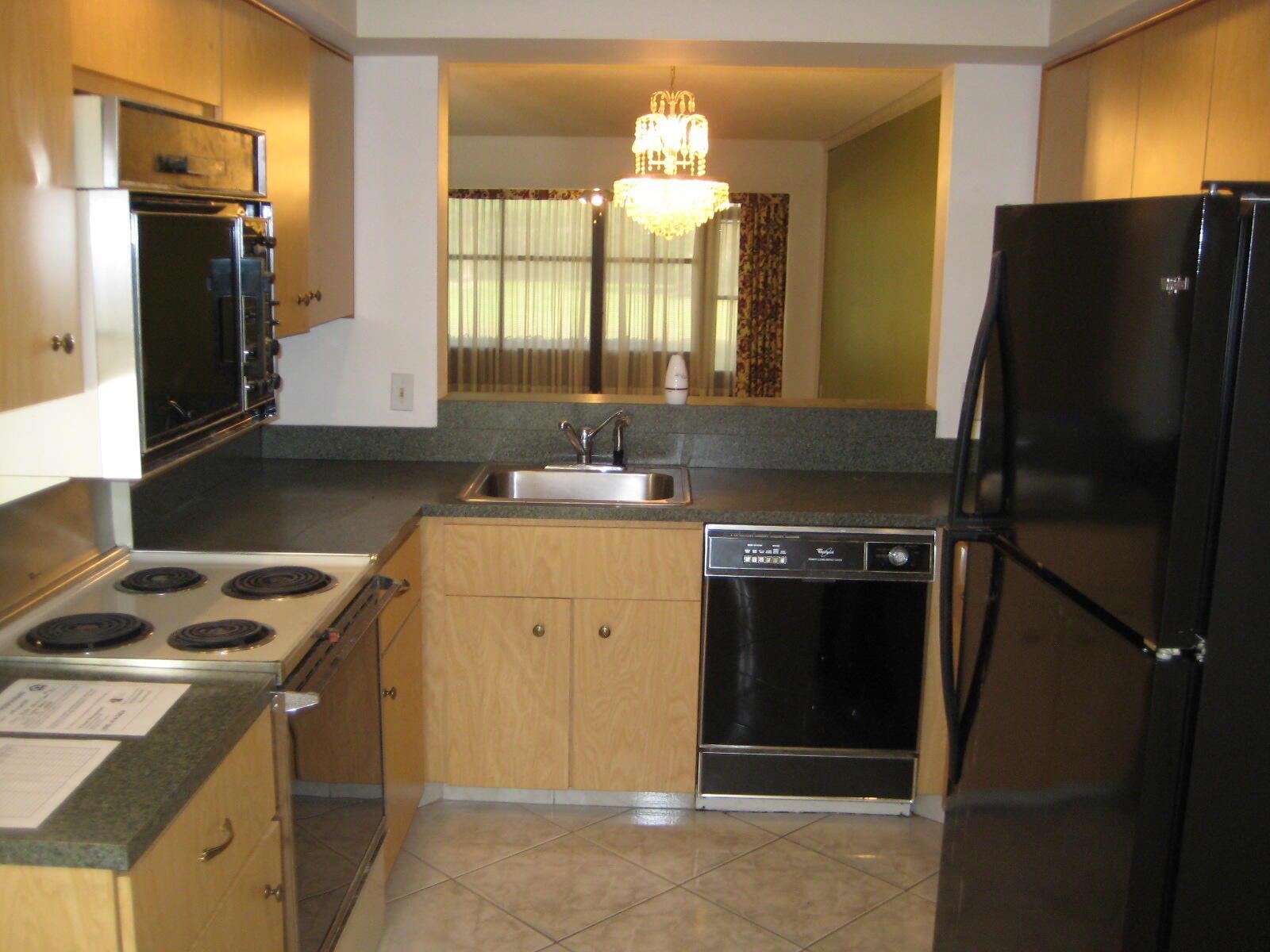 A kitchen features light wood cabinets, dark countertops, black appliances, and a pass-through window — 5153 Oak Hill Road # 511, Delray Beach FL 33484, DELRAY BEACH, FL