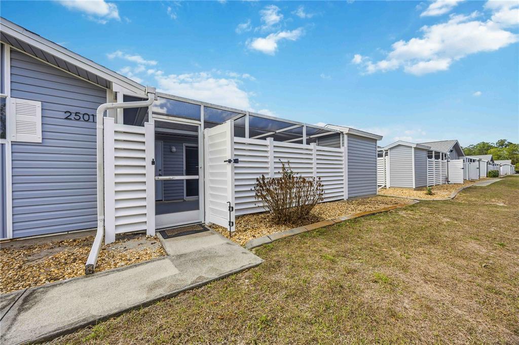 A blue-sided house features a screened-in entryway with white privacy fencing and a gravel border — 3300 LOVELAND BOULEVARD UNIT 2501, PUNTA GORDA, FL
