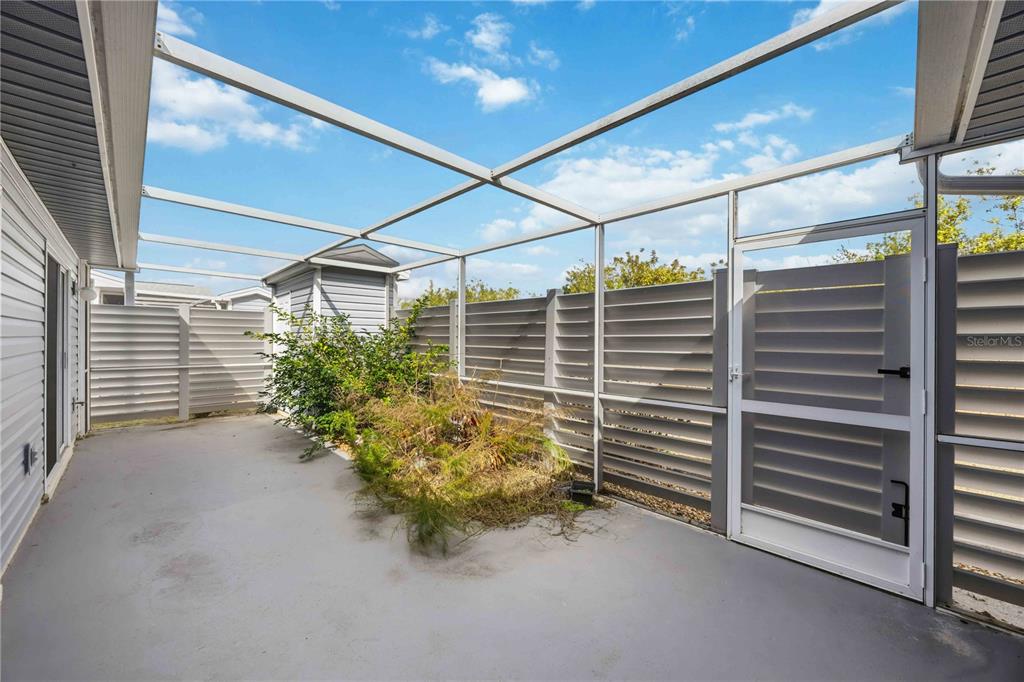 A screened-in patio features a concrete floor, a small garden bed, and privacy fencing — 3300 LOVELAND BOULEVARD UNIT 2501, PUNTA GORDA, FL