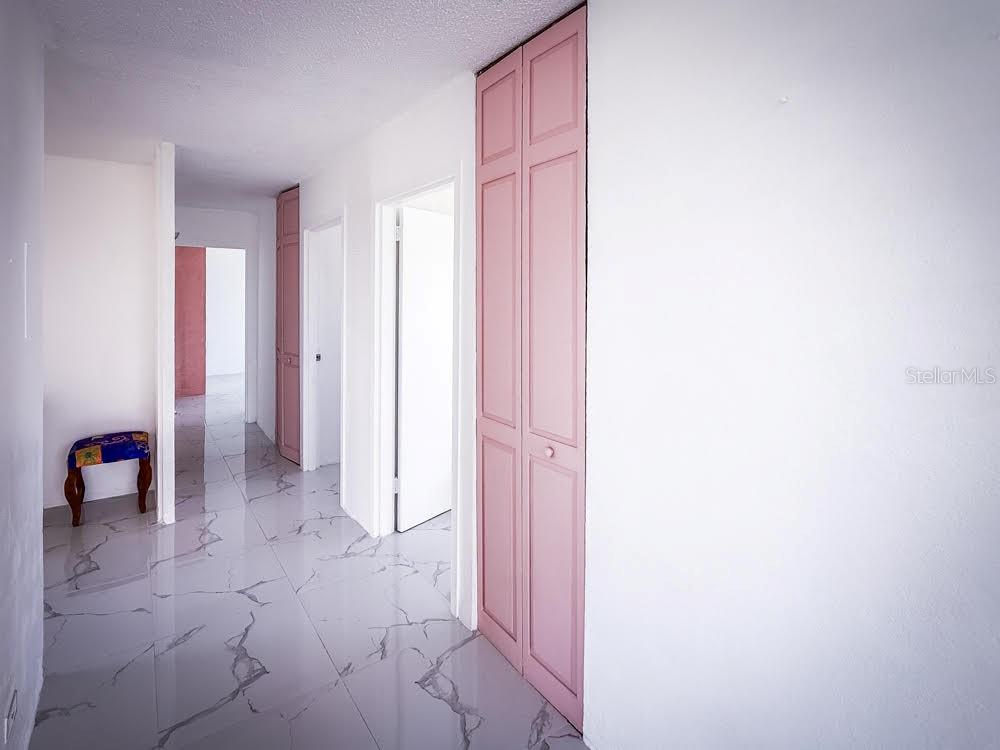 A hallway features white walls, light-colored marble-patterned tile flooring, and pink bi-fold closet doors — MIRAMAR TOWERS 721 HERNANDEZ ST. UNIT A, SAN JUAN, PR