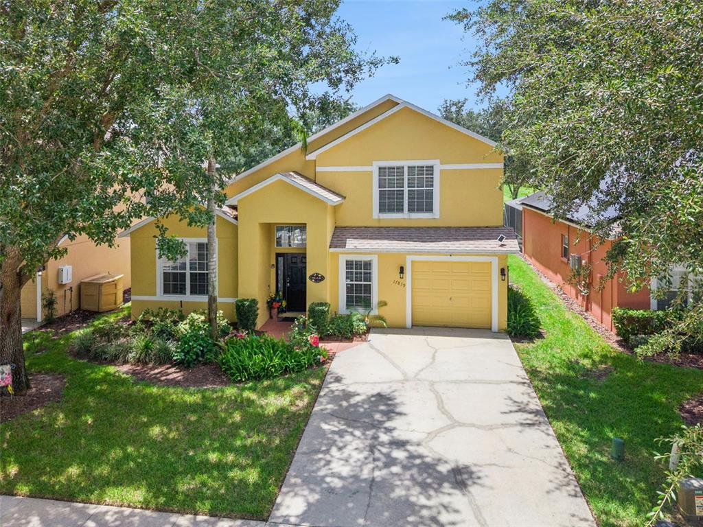 A yellow two-story suburban house features a concrete driveway and a front-facing garage — 17839 WOODCREST WAY, CLERMONT, FL
