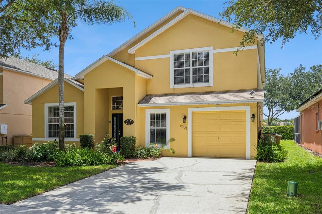 A two-story yellow house with a single-car garage and a concrete driveway — 17839 WOODCREST WAY, CLERMONT, FL