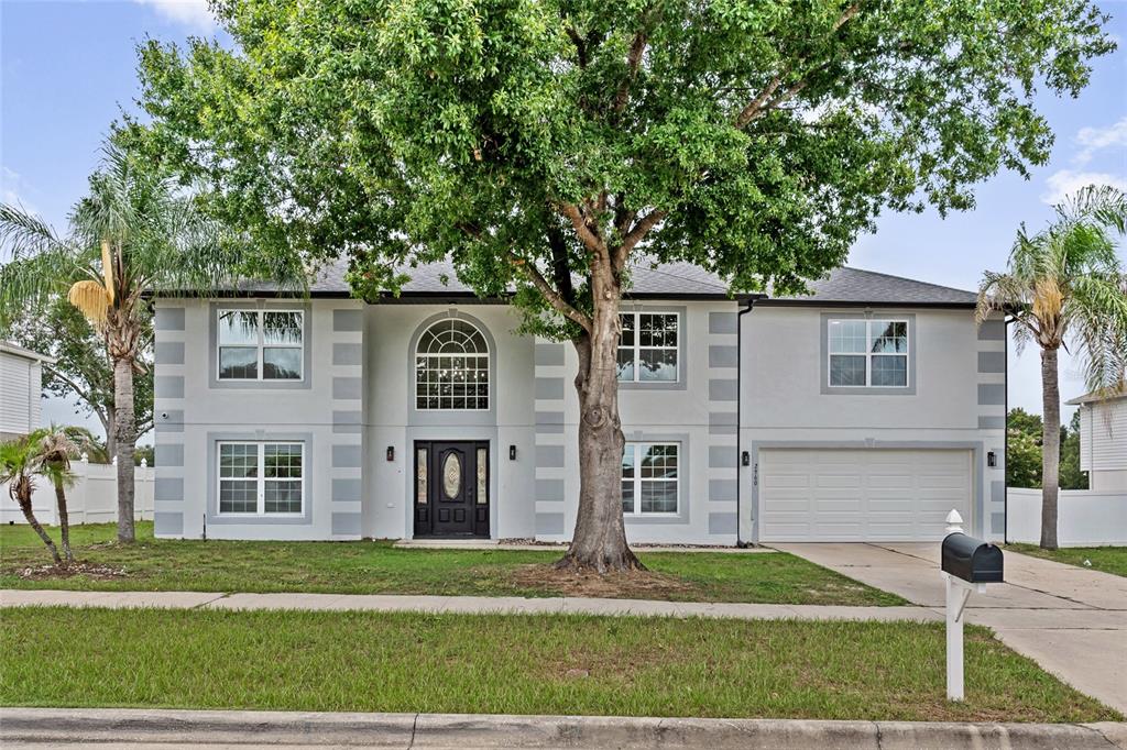 A two-story house with a gray stucco exterior, a large tree, and a two-car garage — 2960 WHITE MAGNOLIA LOOP, CLERMONT, FL