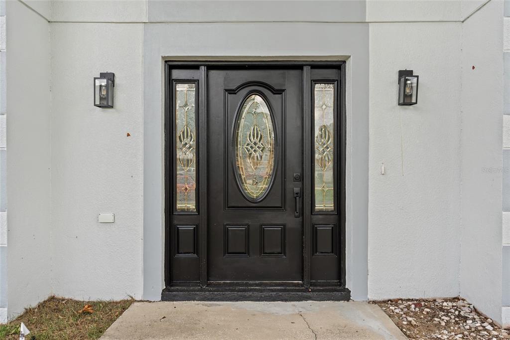 A black front door with an oval glass insert and two sidelights on a white wall — 2960 WHITE MAGNOLIA LOOP, CLERMONT, FL
