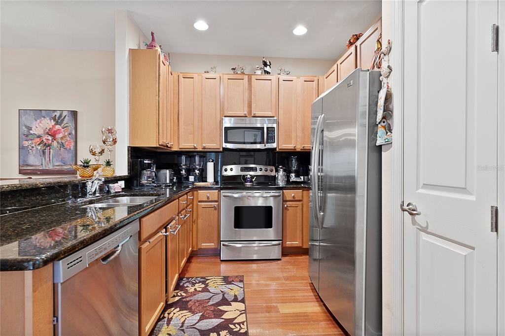 A kitchen features light wood cabinets, stainless steel appliances, and dark granite countertops — 3173 AQUA VIRGO LOOP UNIT 18, ORLANDO, FL