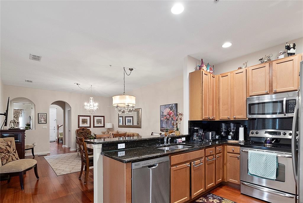 A kitchen with wood cabinets and granite countertops overlooks an adjacent dining area — 3173 AQUA VIRGO LOOP UNIT 18, ORLANDO, FL