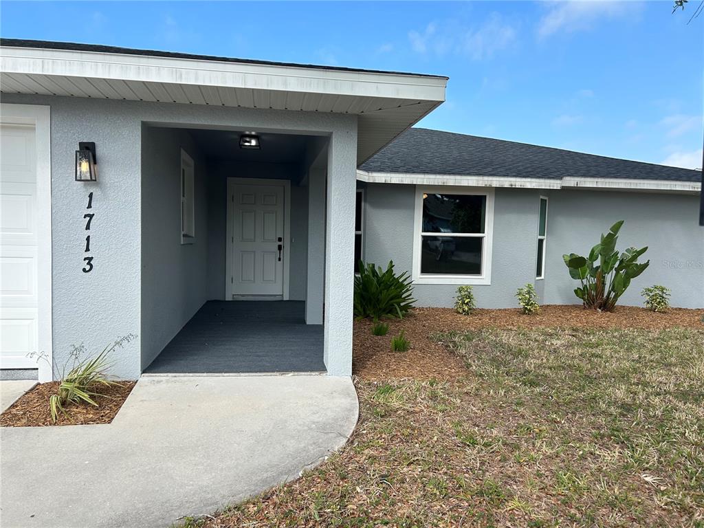 The exterior of a gray house features a covered entryway, a white door, and landscaping — 1713 WALDEN COURT, ENGLEWOOD, FL