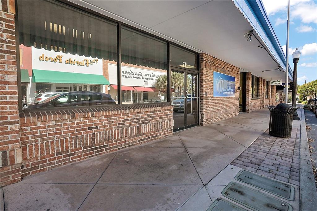 The exterior of a brick commercial building features large windows, a glass door, and sidewalk — 711 W MAIN STREET, LEESBURG, FL