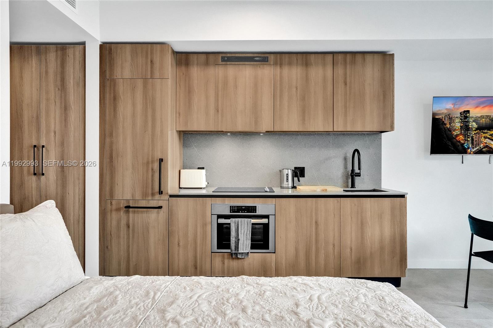 A studio apartment features a kitchenette with wood-grain cabinets, stainless steel appliances, and a bed — 121 NE 5th Street # 1404, Miami FL 33132, MIAMI, FL