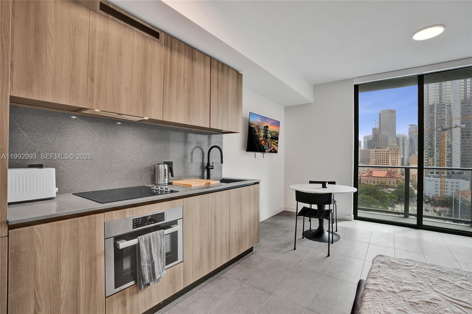 A modern kitchen with wood cabinets and a dining area overlooks a city skyline — 121 NE 5th Street # 1404, Miami FL 33132, MIAMI, FL