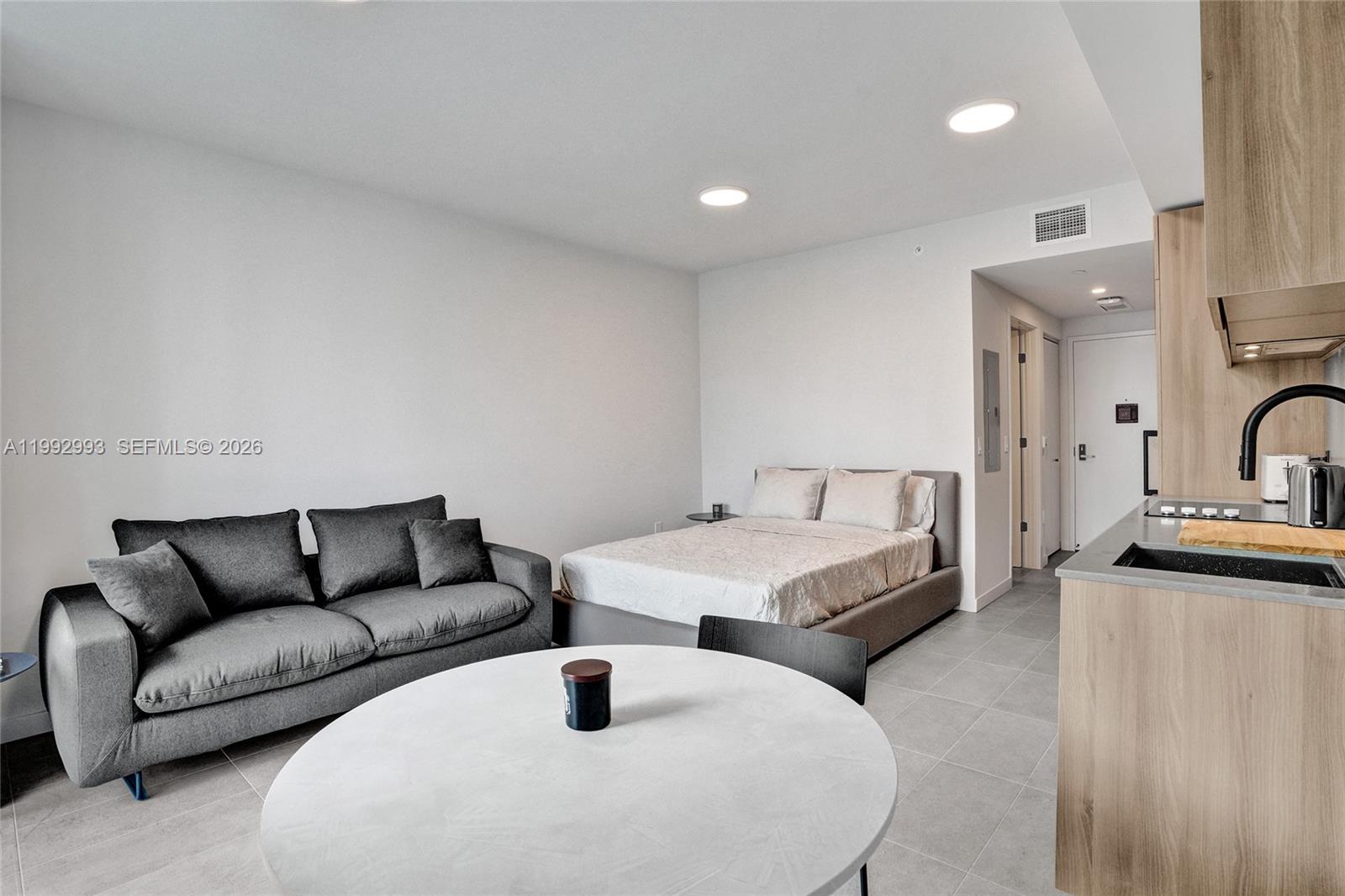 A studio apartment features a gray sofa, a bed, and a kitchen with wood cabinetry — 121 NE 5th Street # 1404, Miami FL 33132, MIAMI, FL