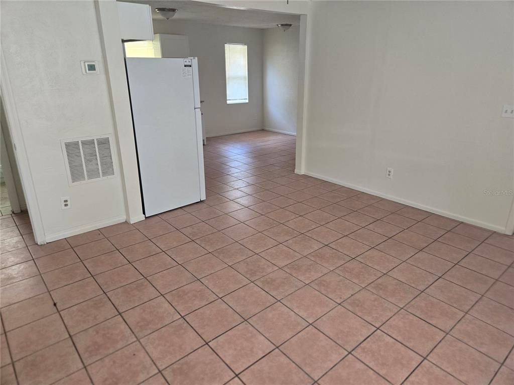 A room with light-colored walls and brown tiled flooring features a white refrigerator — 843 41ST STREET S, ST PETERSBURG, FL