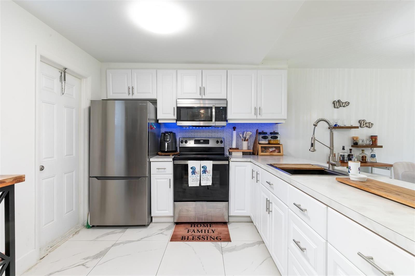 A kitchen features white cabinets, stainless steel appliances, marble-look tile flooring, and a blue backsplash — 600 NE 2nd Street # 105, Dania Beach FL 33004, DANIA BEACH, FL