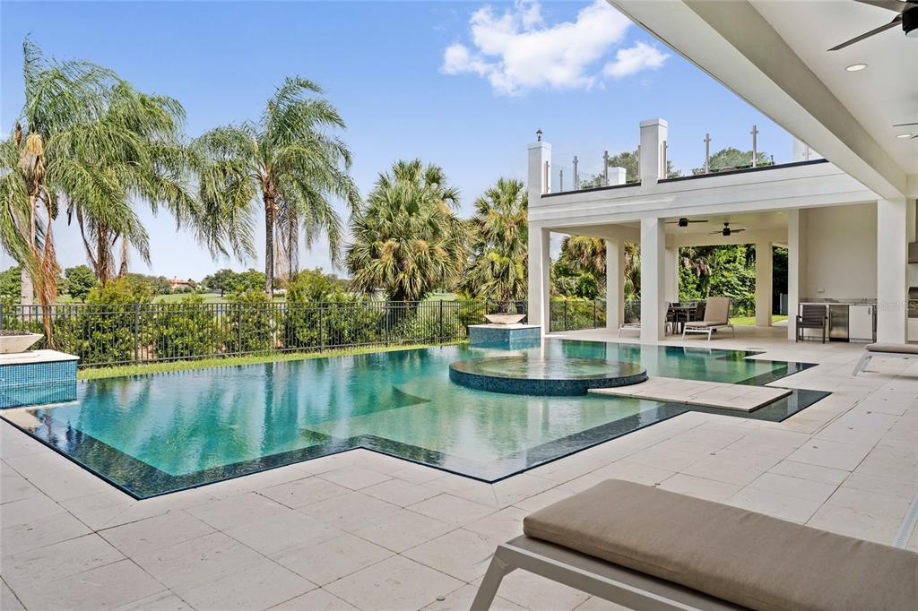 A modern swimming pool with an integrated spa sits on a patio beside a covered lanai — 6159 HARBOUR TOWN COURT, ORLANDO, FL