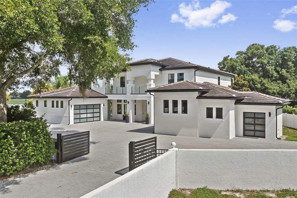 A two-story white house with a tile roof, glass garage doors, and a gated driveway — 6159 HARBOUR TOWN COURT, ORLANDO, FL