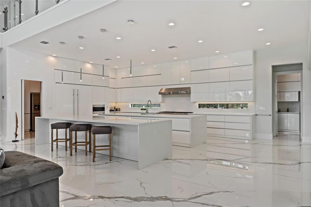A modern white kitchen features a large island with bar stools and marble tile flooring — 6159 HARBOUR TOWN COURT, ORLANDO, FL