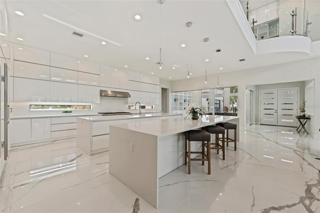 A modern white kitchen features a large waterfall island, glossy cabinetry, and marble-patterned tile flooring — 6159 HARBOUR TOWN COURT, ORLANDO, FL