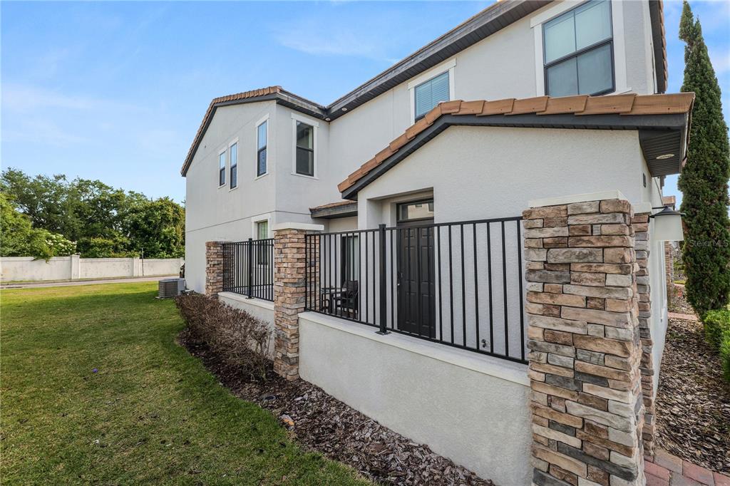 The exterior of a two-story house features a stone-accented patio enclosed by a black fence — 129 KENNY BOULEVARD, HAINES CITY, FL