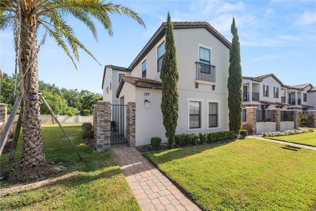 A two-story townhouse with a stone-accented entryway, a brick walkway, and two tall cypress trees — 129 KENNY BOULEVARD, HAINES CITY, FL