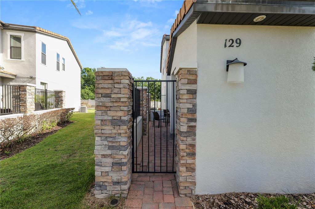 A stone-pillared gate leads to a paved side patio between two residential buildings — 129 KENNY BOULEVARD, HAINES CITY, FL