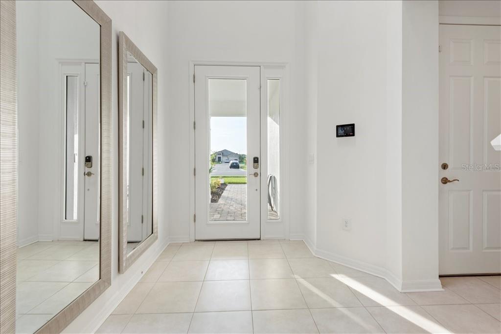 A bright entryway features white walls, tile flooring, two large mirrors, and a glass-paneled front door — 17703 SAVORY MIST CIRCLE, LAKEWOOD RANCH, FL