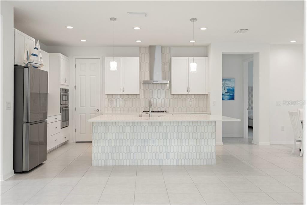 A modern white kitchen features a large island, stainless steel appliances, and picket-style tile backsplashes — 17703 SAVORY MIST CIRCLE, LAKEWOOD RANCH, FL