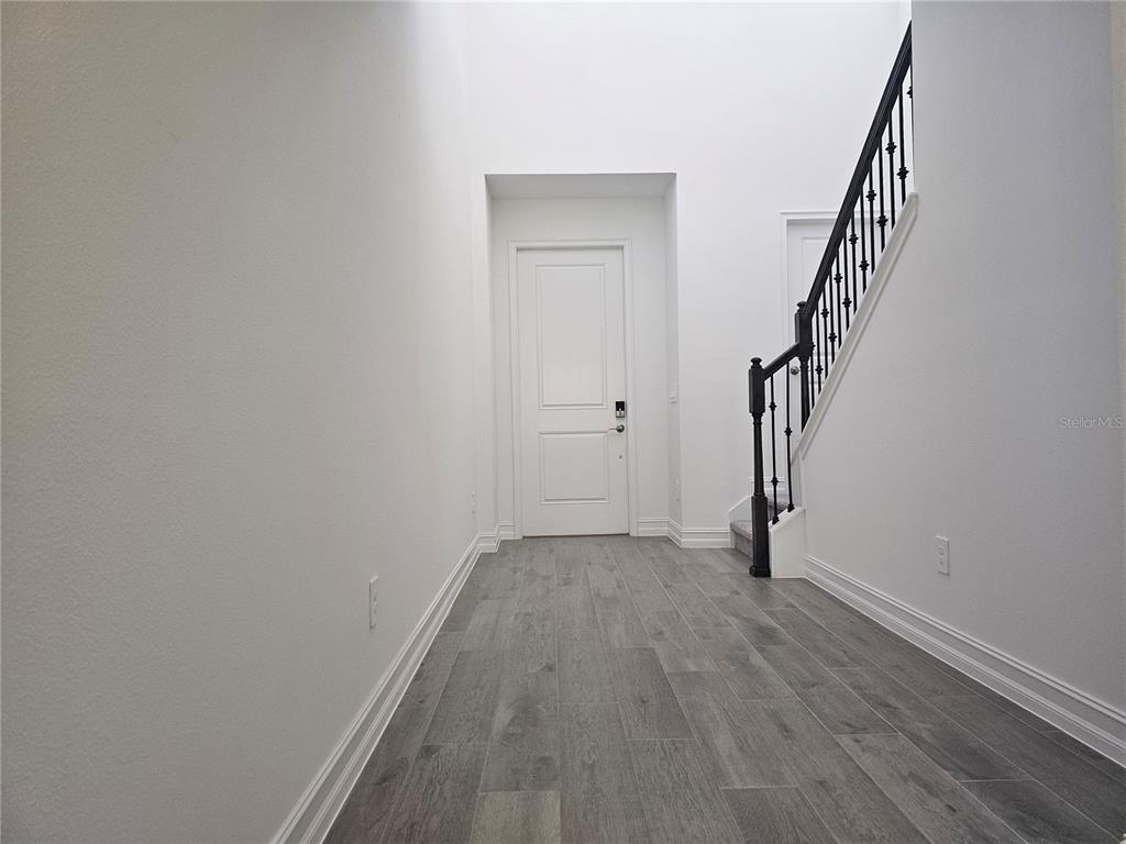 A bright entryway features gray wood-look flooring, white walls, and a staircase with black railings — 18271 PEARL VIEW PLACE, LUTZ, FL