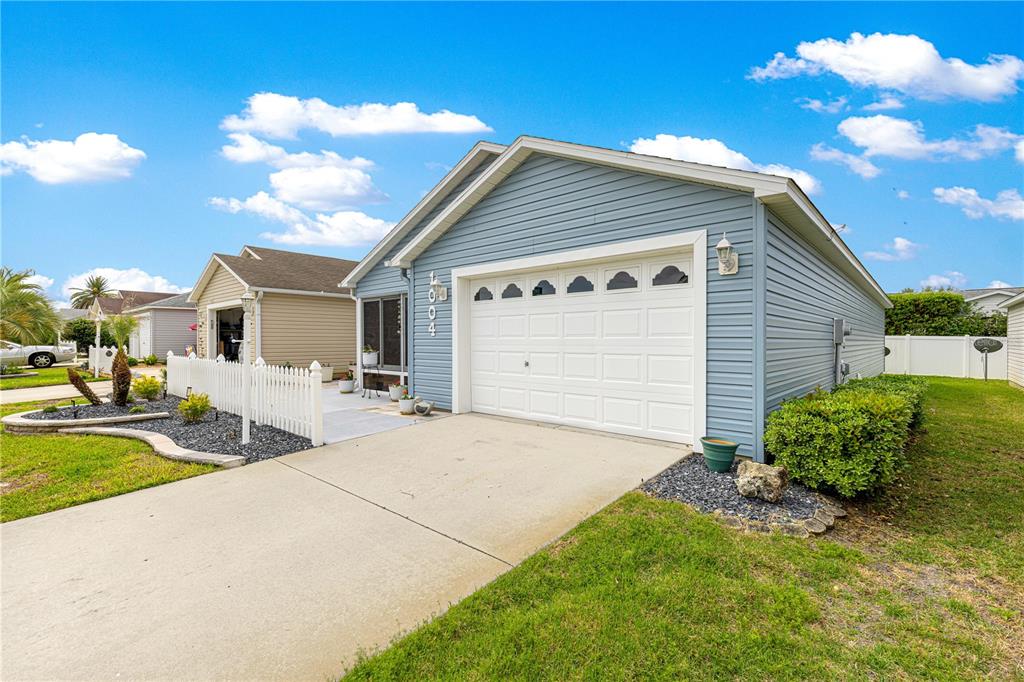A blue-sided house with a white garage door and a small front patio area — 1004 DAVIT PLACE, THE VILLAGES, FL
