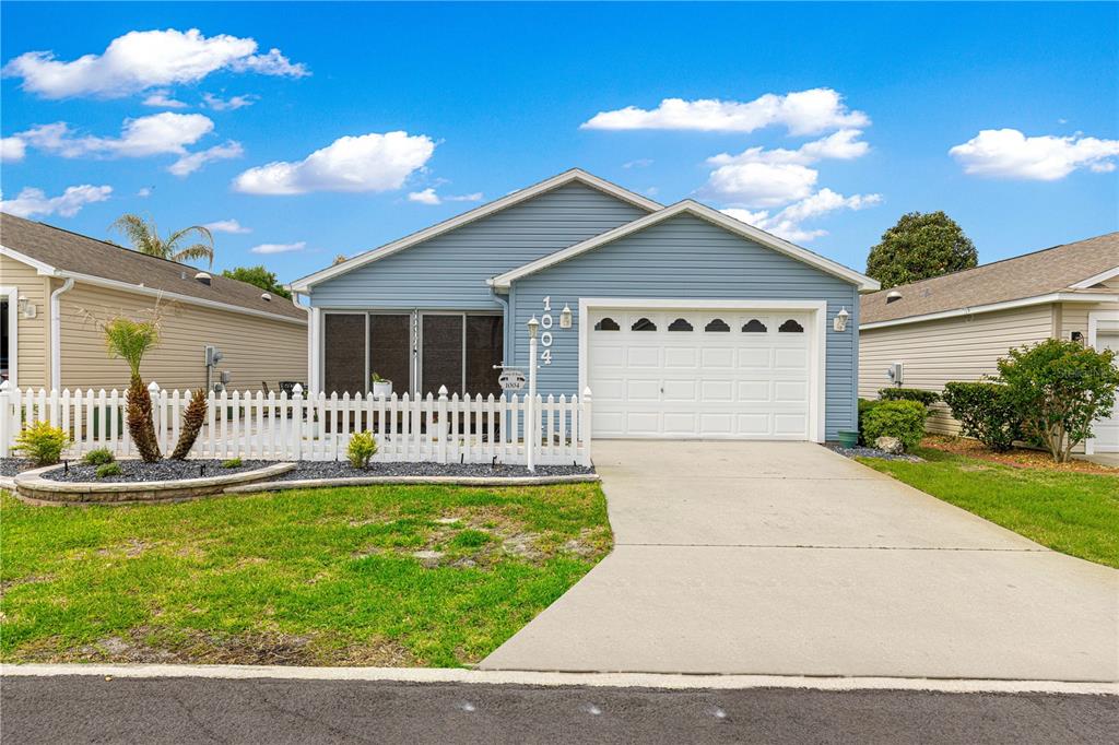 A blue single-story house with a white picket fence, a garage, and a screened porch — 1004 DAVIT PLACE, THE VILLAGES, FL