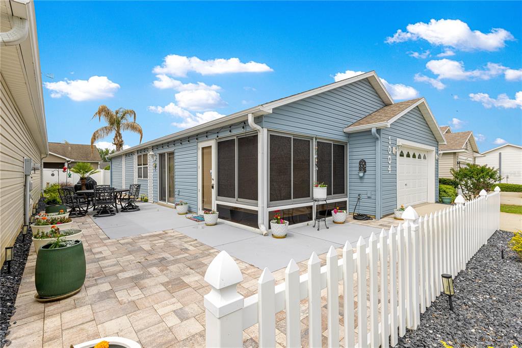 A light blue house with a screened-in porch, paver patio, and white picket fence — 1004 DAVIT PLACE, THE VILLAGES, FL