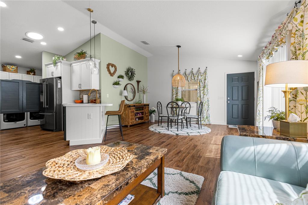 An open-concept living and dining area features wood-look flooring, a kitchen island, and light-colored walls — 1004 DAVIT PLACE, THE VILLAGES, FL