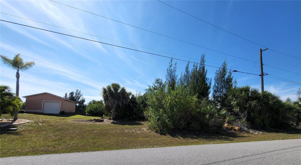 A vacant, grassy lot with trees and shrubs sits next to a house with a garage — 9598 SPRING CIRCLE, PORT CHARLOTTE, FL