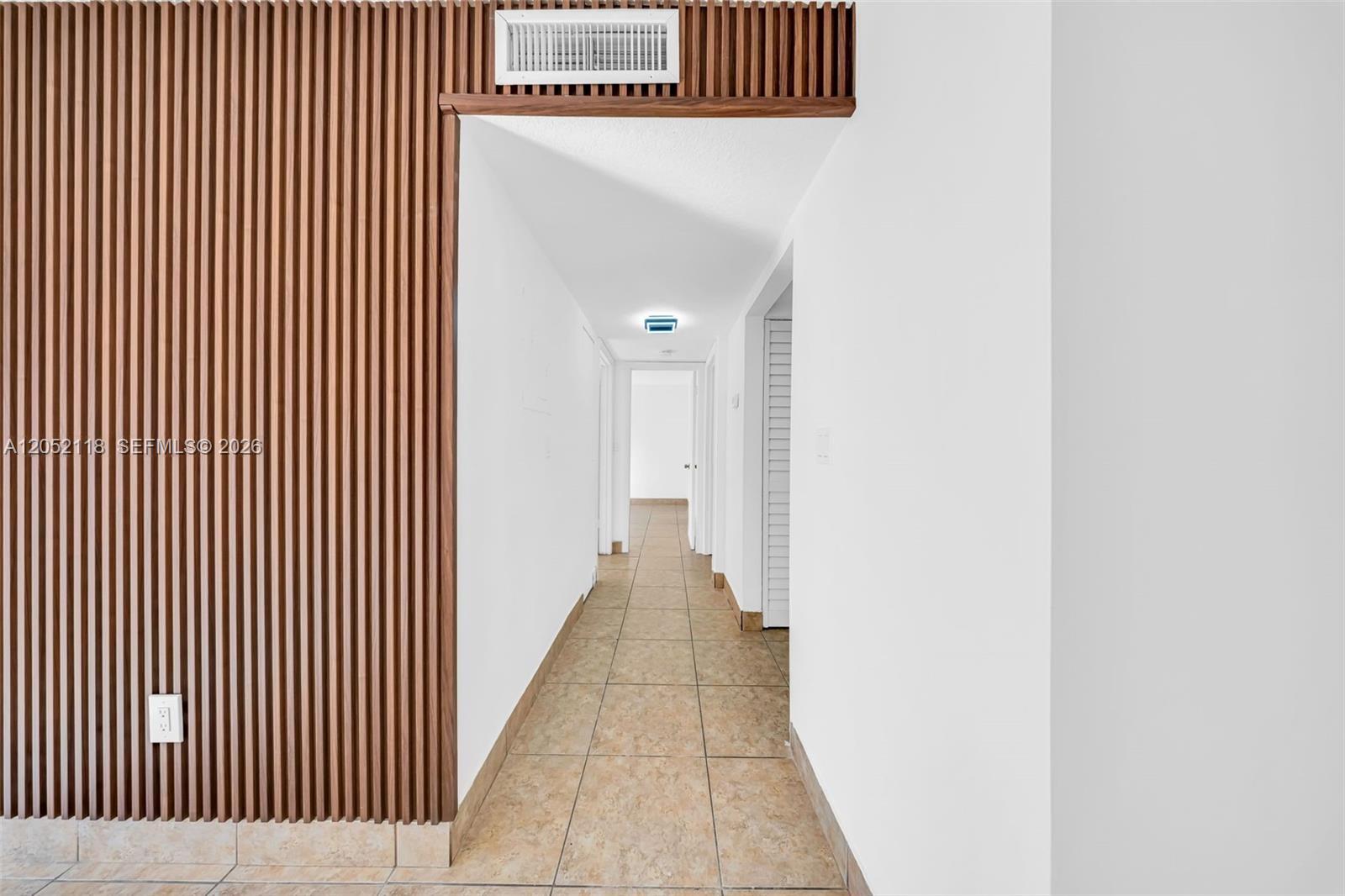 A hallway features a wood-slatted accent wall, tile flooring, and white walls — 8145 NW 7th St # 111, Miami FL 33126, MIAMI, FL
