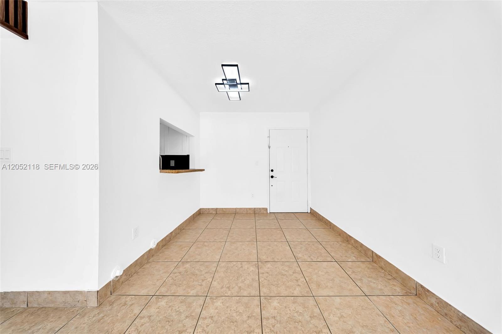 An empty room features white walls, tan tile flooring, a pass-through window, and a ceiling light — 8145 NW 7th St # 111, Miami FL 33126, MIAMI, FL