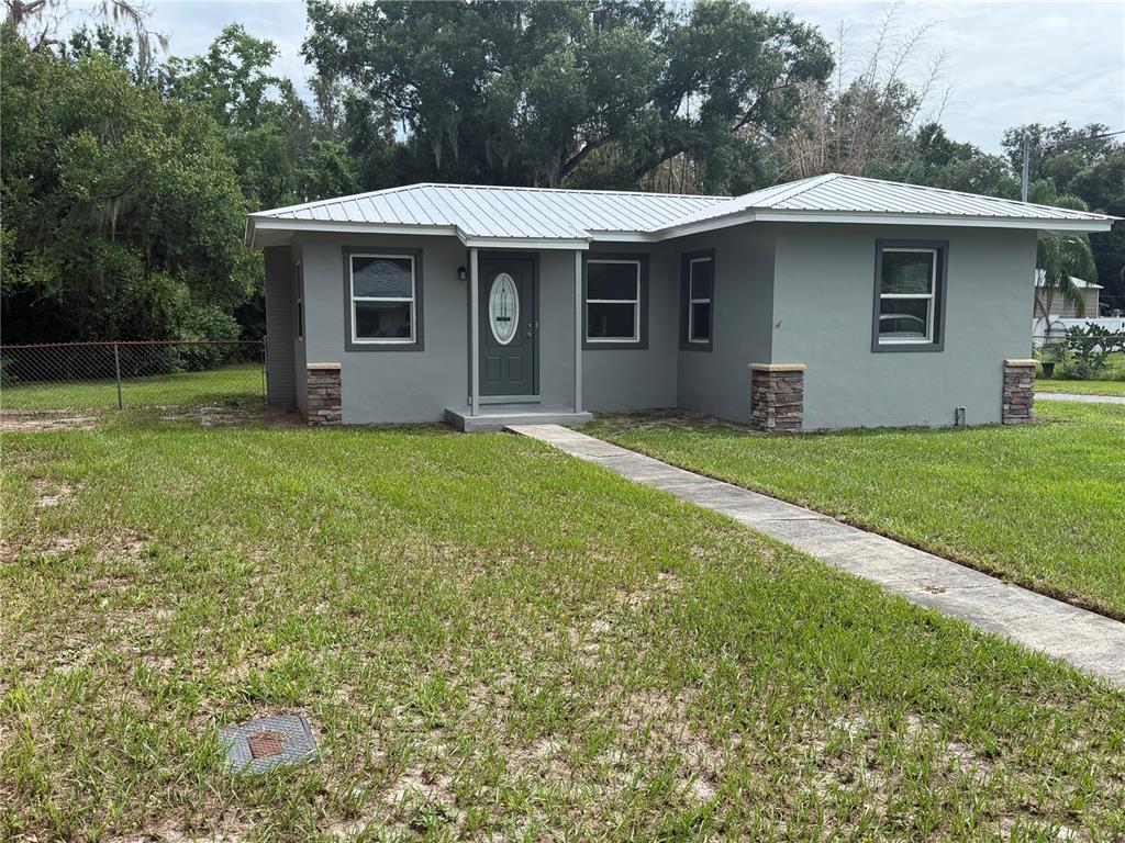 A gray single-story house with a metal roof and stone-accented pillars stands on a lawn — 1986 AVENUE F, WINTER HAVEN, FL