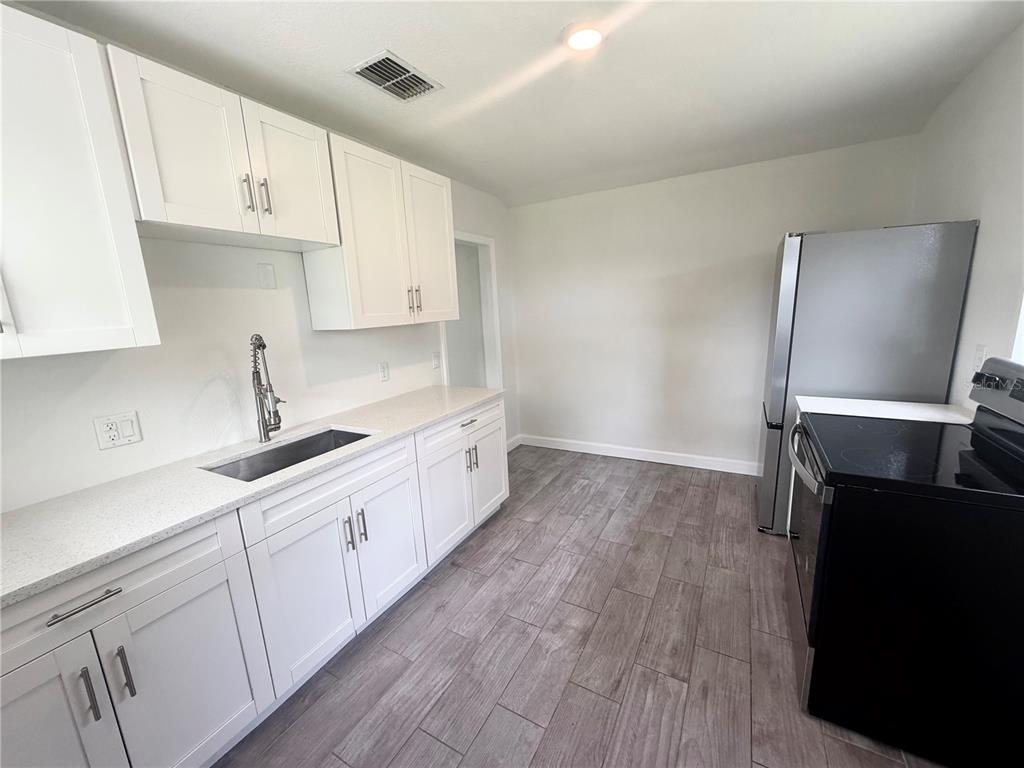 A kitchen with white cabinets, light countertops, stainless steel appliances, and wood-look tile flooring — 1986 AVENUE F, WINTER HAVEN, FL