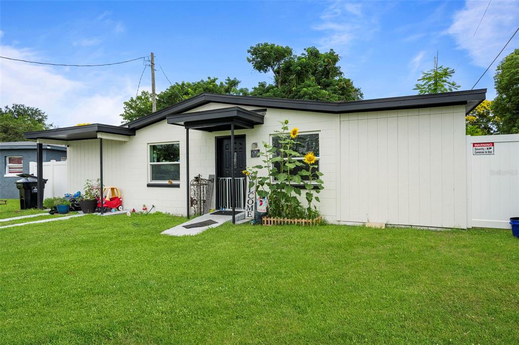 A single-story white house with a black roof, front porch, and sunflowers in the yard — 4333 ARCH STREET, ORLANDO, FL