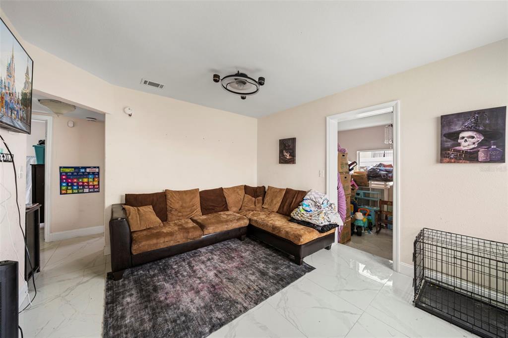 A living room features a brown sectional sofa, a dark area rug, and white tile flooring — 4333 ARCH STREET, ORLANDO, FL