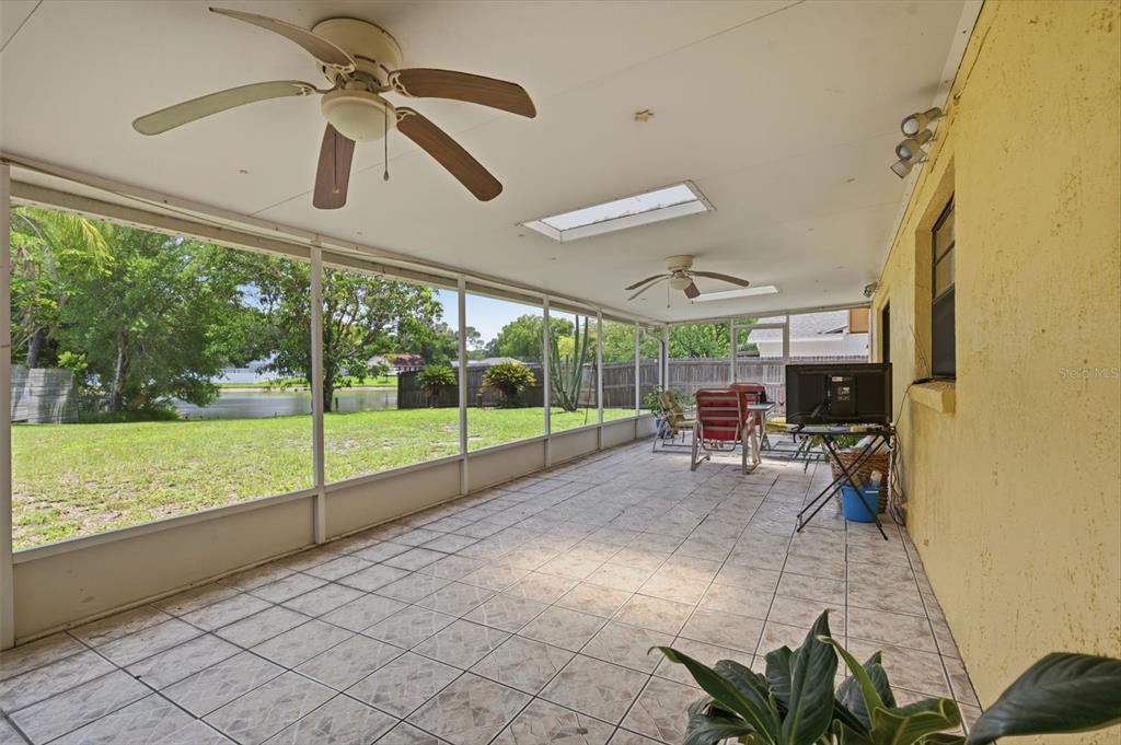 A screened-in patio with tiled flooring, two ceiling fans, and a view of a yard — 15806 PENNINGTON ROAD, TAMPA, FL