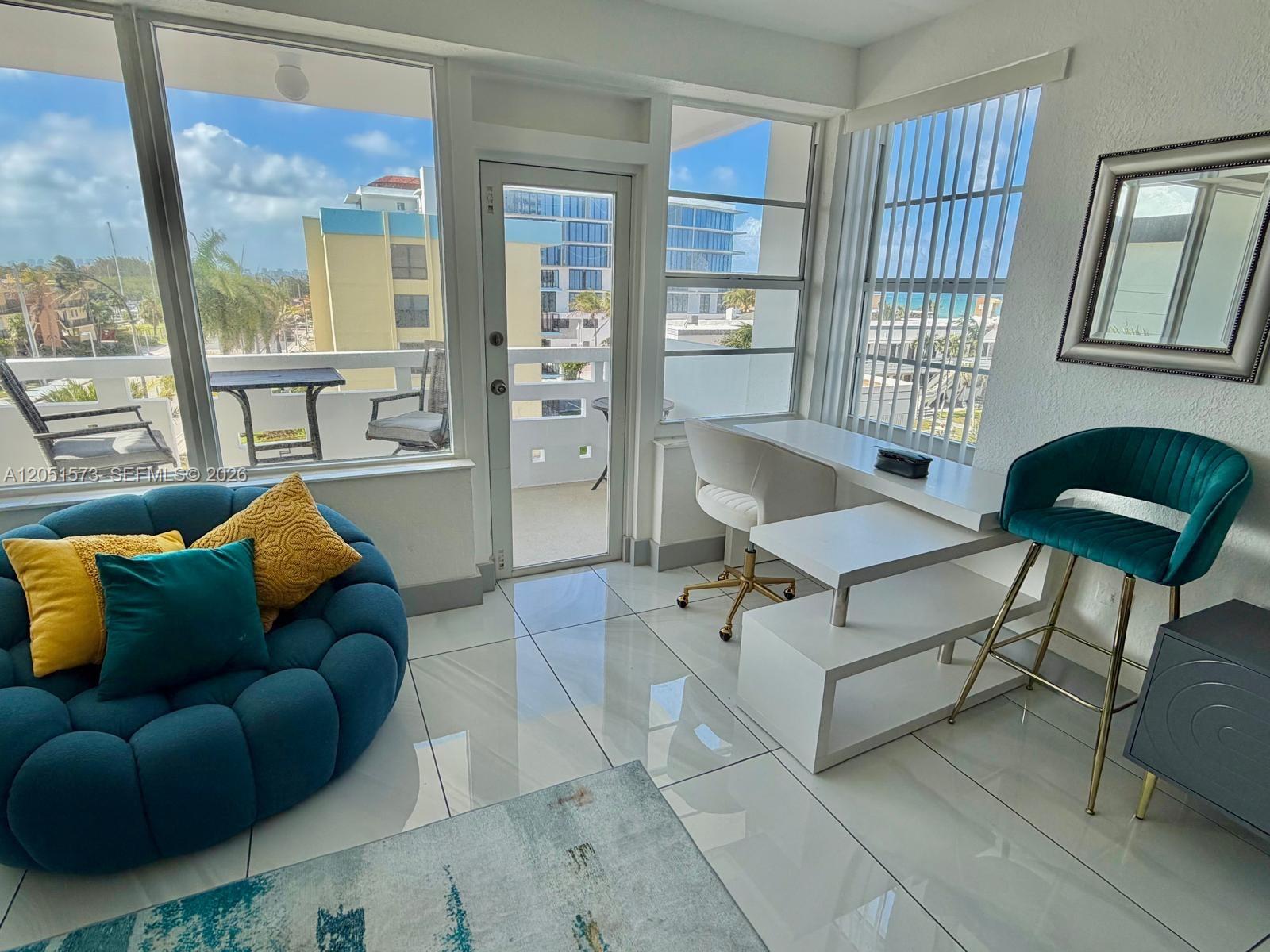 A bright room features a blue circular sofa, a white desk, and a balcony view — 3111 N Ocean Dr # 401, Hollywood FL 33019, HOLLYWOOD, FL