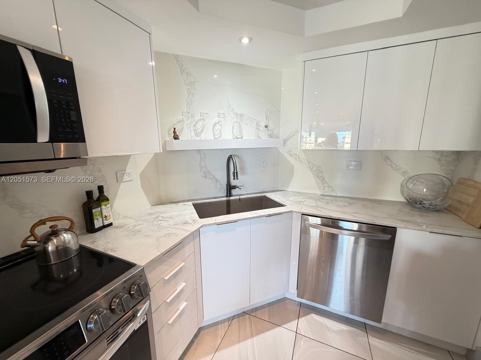 A modern kitchen features white cabinets, marble-patterned countertops, stainless steel appliances, and tile flooring — 3111 N Ocean Dr # 401, Hollywood FL 33019, HOLLYWOOD, FL