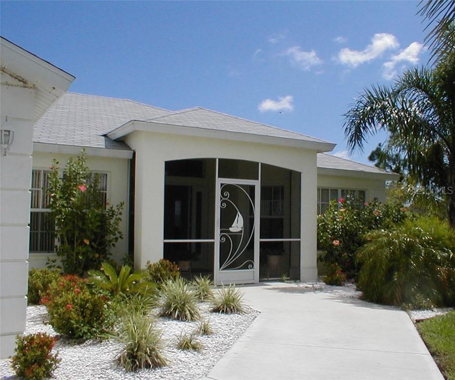 A white house exterior features a screened-in front entryway with a decorative sailboat door — 15001 APPLETON BLVD, PORT CHARLOTTE, FL