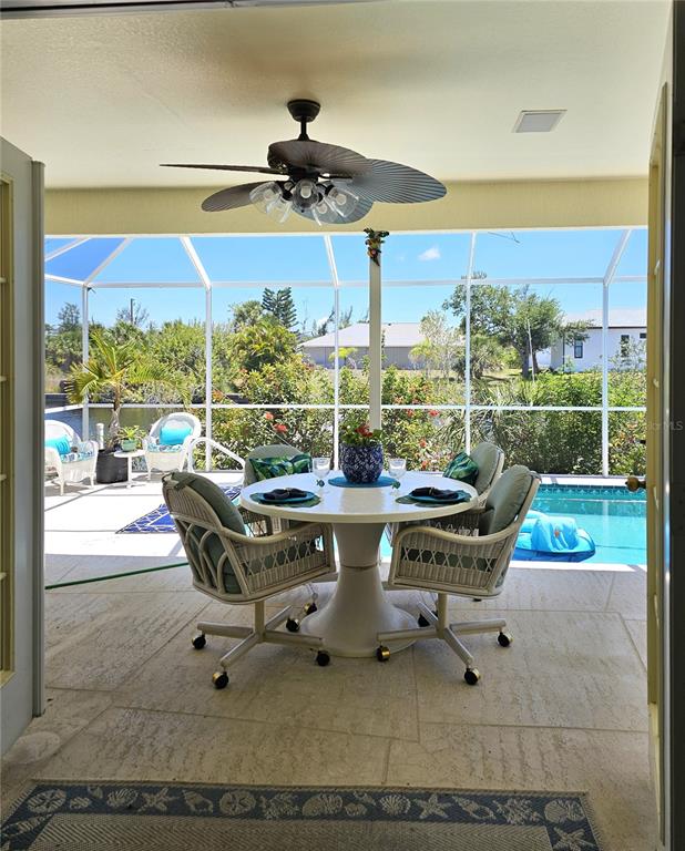 A covered patio features a dining set, ceiling fan, and a screened-in pool area — 15001 APPLETON BLVD, PORT CHARLOTTE, FL