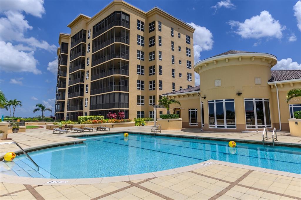 A multi-story tan apartment building stands behind a swimming pool with a tiled deck — 3313 SUNSET KEY CIR UNIT 701, PUNTA GORDA, FL